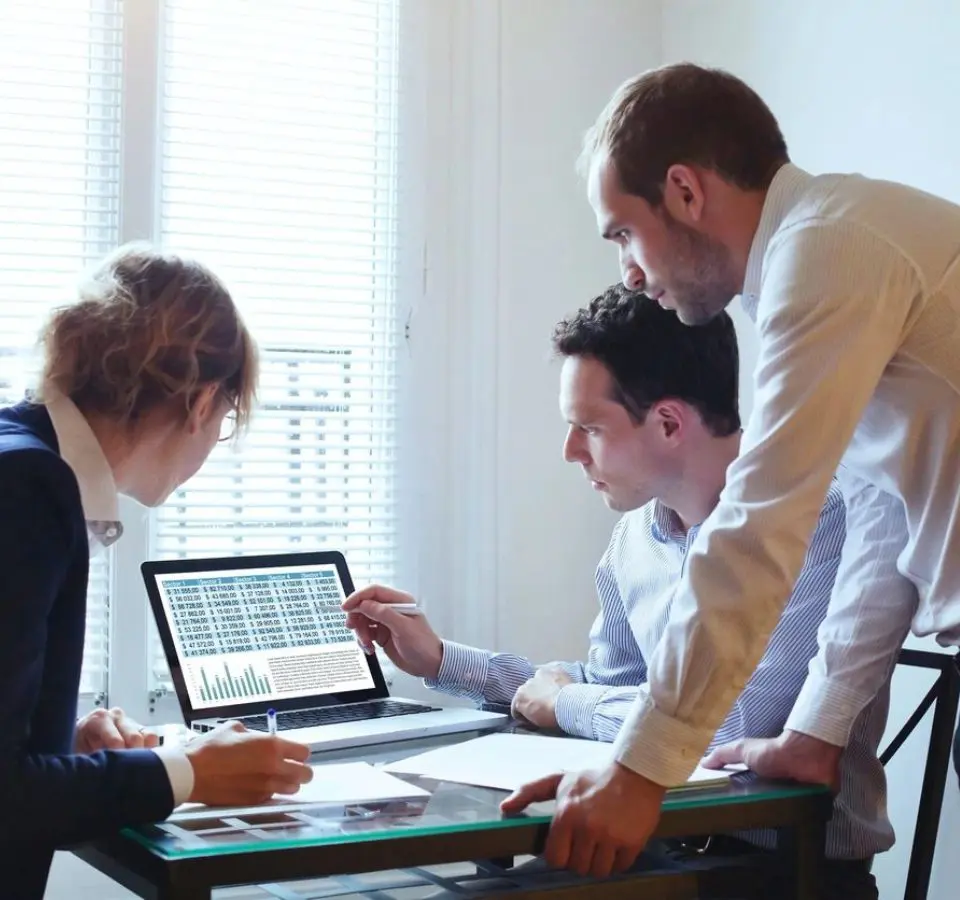 Three men are looking at a laptop screen.